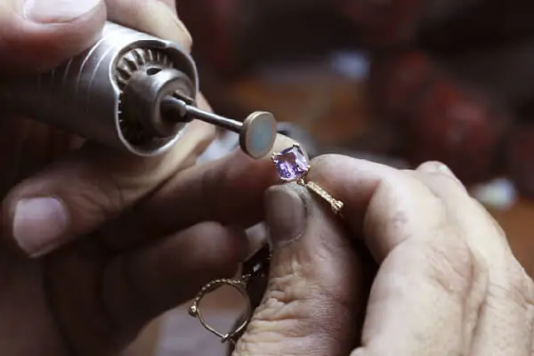A piece of gold jewellery with a prong set pink crystal is being assembled