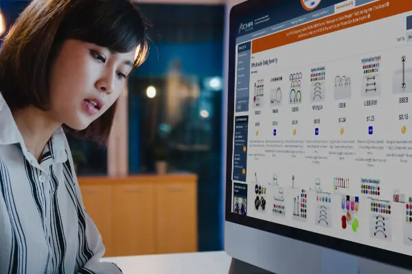 A young Asian woman wearing a blouse is looking at a computer screen on which piercing jewellery is visible