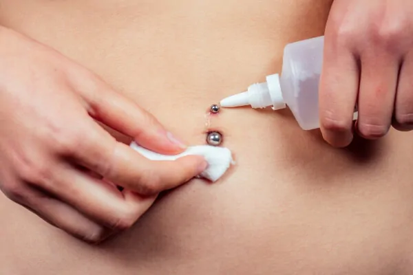 A woman cleaning her belly button piercing using saline solution and a piece of cotton wool