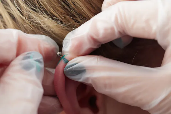 A piece of ear jewellery is being inserted by white gloved hands
