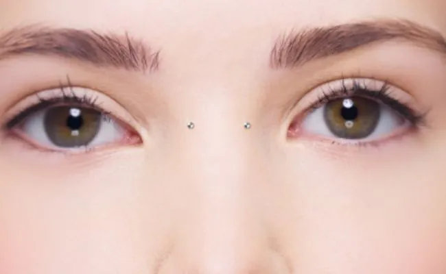 The upper face of a woman, the nose bridge being adorned with a bridge piercing