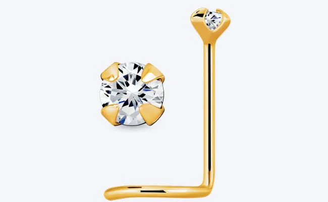 A gold L-shaped nose stud with a prong set transparent crystal top