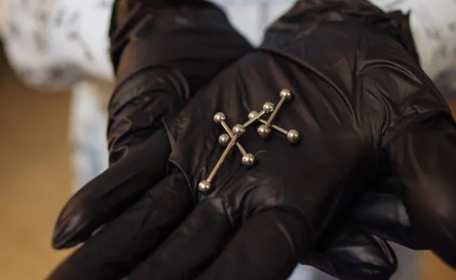 Black gloved hands are holding five pieces of barbell jewellery