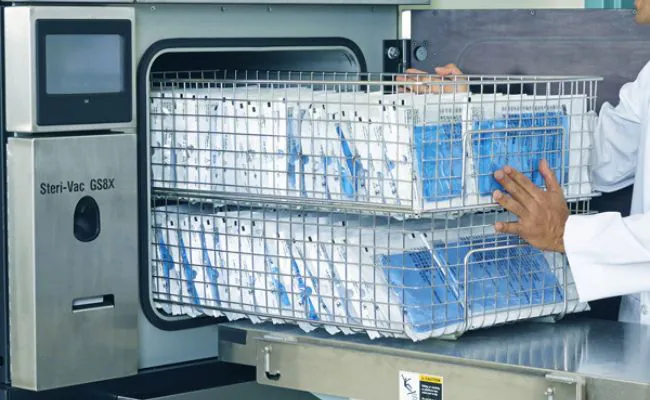 An open autoclave machine with a removed tray tightly packed with vacuum sealed envelopes