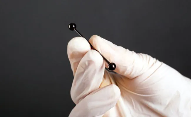 A white gloved hand is holding up a black piercing barbell