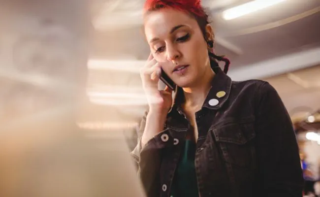 A red haired woman with several facial piercings is talking on a mobile phone