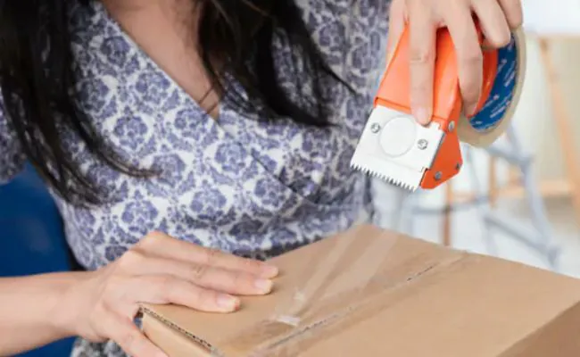 A woman with long black hair is taping a box