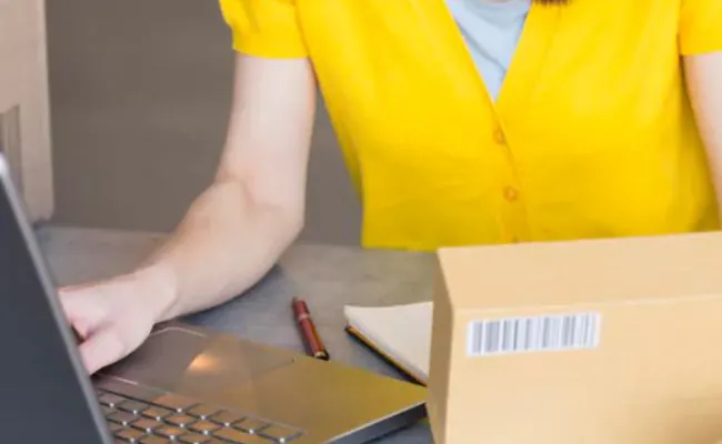 A woman with black hair and a yellow blouse is working on a laptop
