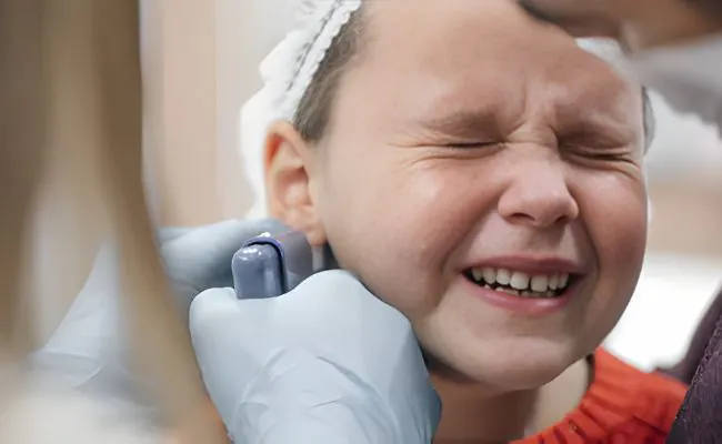 A young girl with eyes closed is crying while getting her earlobe pierced with a piercing gun