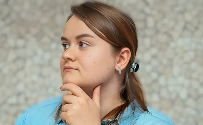 A young pensive looking woman with a ponytail, a blue shirt and an earring