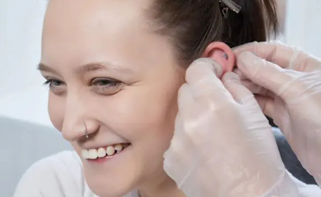 A young woman with a nose ring is smiling while getting a helix piercing