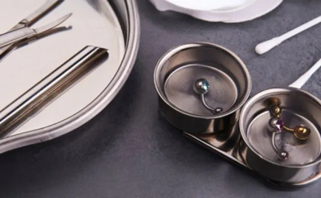 Some curved barbells & piercing tools placed inside different metal trays
