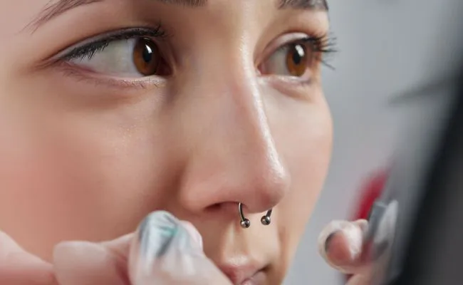 A woman face with a septum piercing wearing a circular barbell