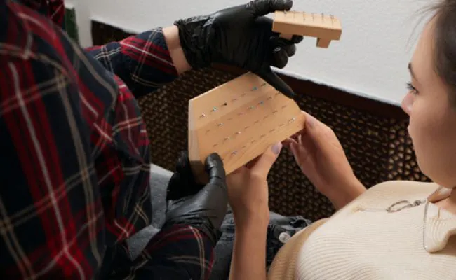 A woman is examining a selection of piercing jewellery on wooden displays