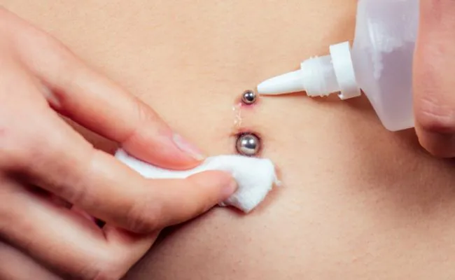 A belly button piercing is being cleaned using saline solution and cotton wool