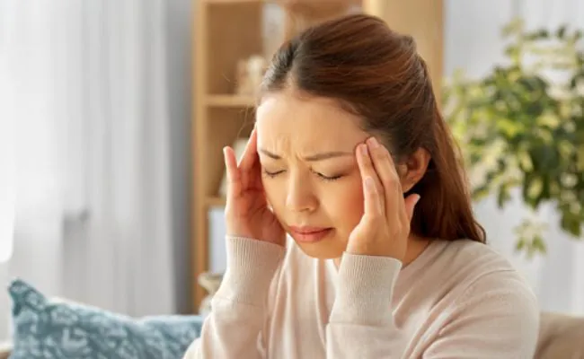 A distressed looking woman with closed eyes is touching her temples