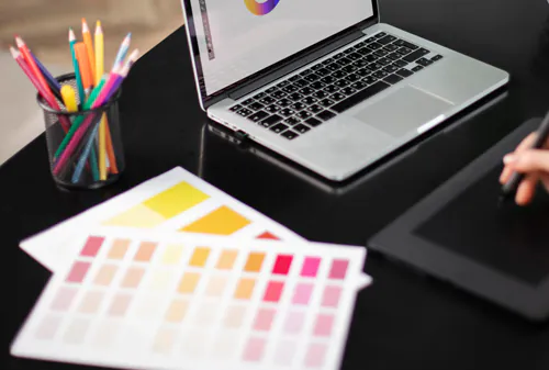 A black table with a notebook, a glass with colour pencils and a few sheets of paper on it