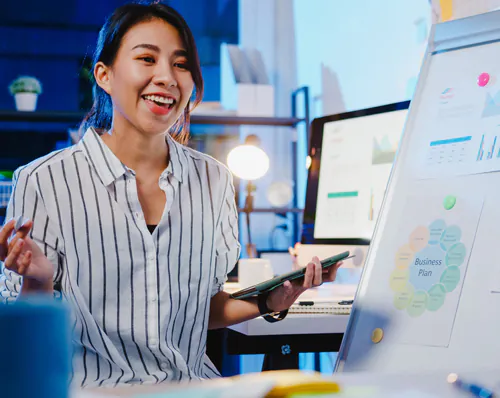 A cheerful and smiling young woman wearing a white striped shirt and holding a tablet in an office environment