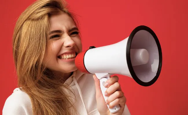A young beautiful woman with long hair is grinning while holding a megaphone to her mouth