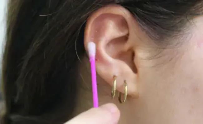 Closeup of an ear with two earrings that is being cleaned using a cotton bud