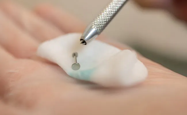 An open hand holding a piece of gauze with a piece of labret jewellery on it