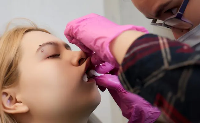 A woman with closed eyes is receiving a medusa piercing from a professional piercer