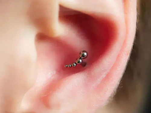 Closeup of an ear, adorned with an earring and a piece of conch piercing jewellery