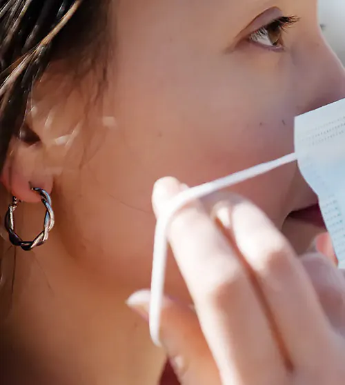 A young woman with a large earring is putting on a face mask