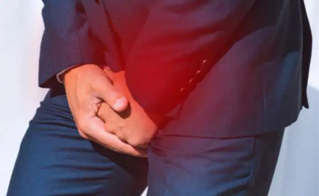 A man with a dark blue suit is clutching his crotch with two hands