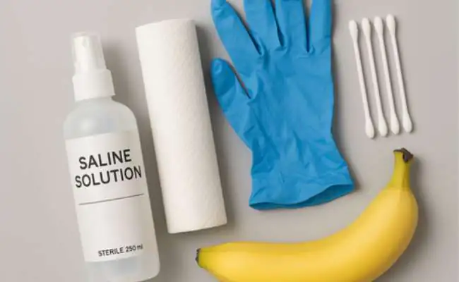 A banana and piercing aftercare supplies including saline solution, a blue glove and cotton buds