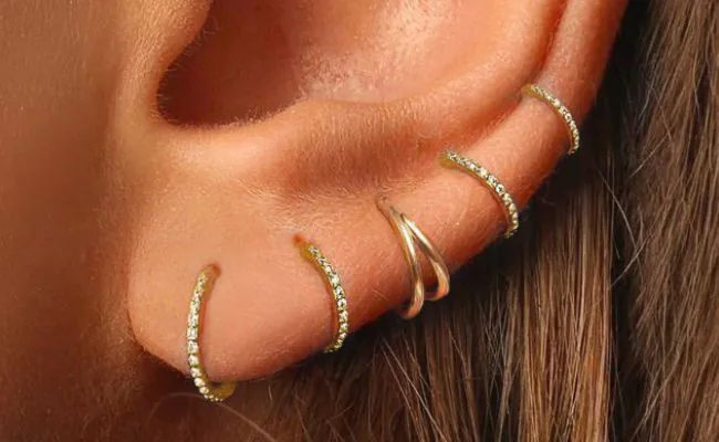 An ear adorned with various ear piercing rings made of gold